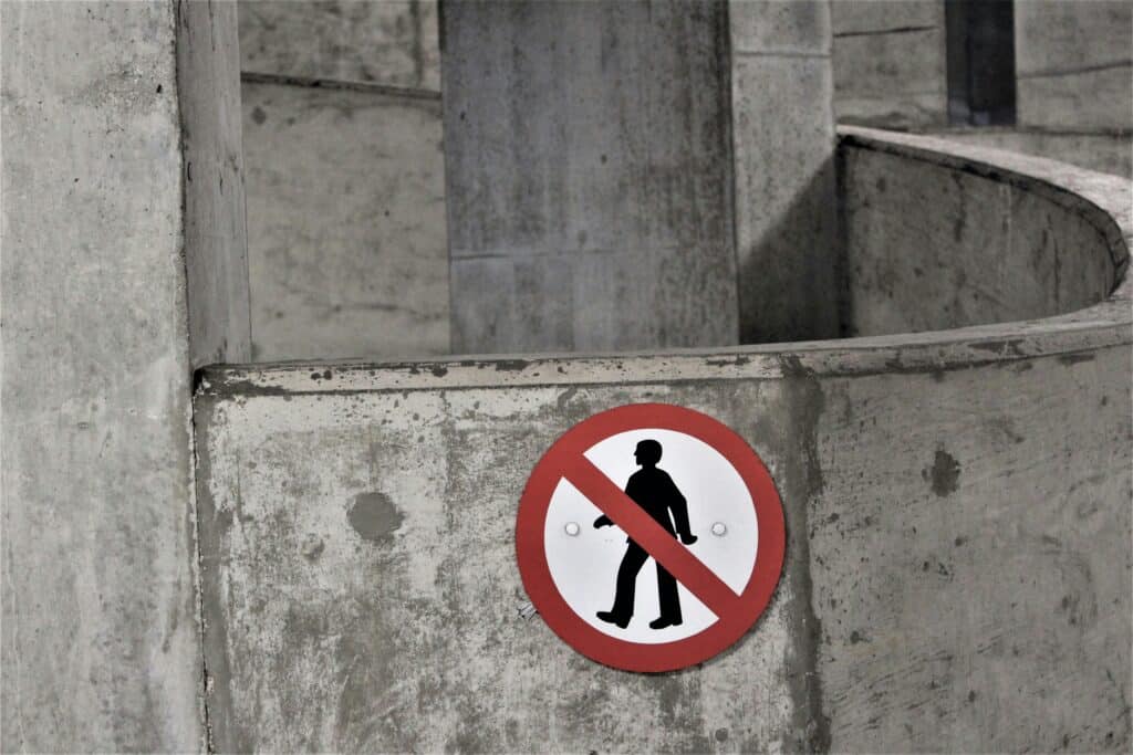 Circular red sign with a crossed-out figure, mounted on a concrete column in a spiral structure, indicating restricted access.