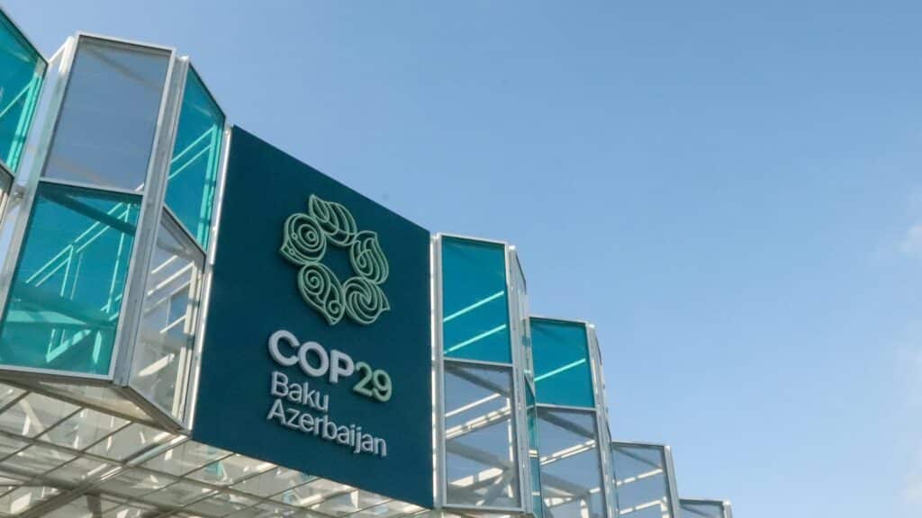 COP29 sign displayed prominently at the Baku venue, featuring teal accents and stylized logo against a clear blue sky.