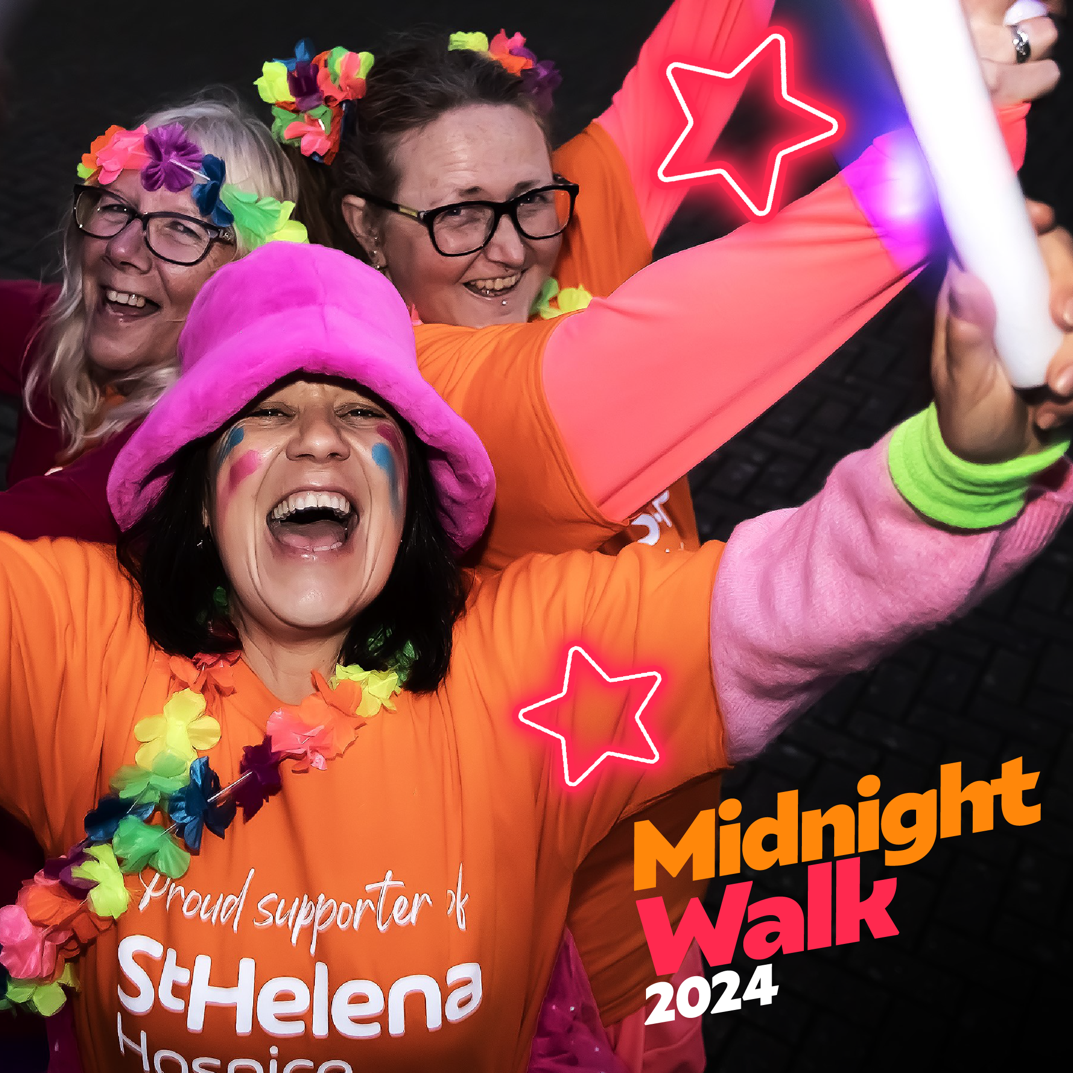 Three smiling women in vibrant, colorful outfits celebrate at the Midnight Walk 2024, surrounded by playful decorations and bright neon stars.