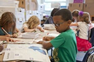 Children engaged in art activities at tables, with a boy in a green shirt writing in a school setting relevant to crisis communications for schools and nurseries.